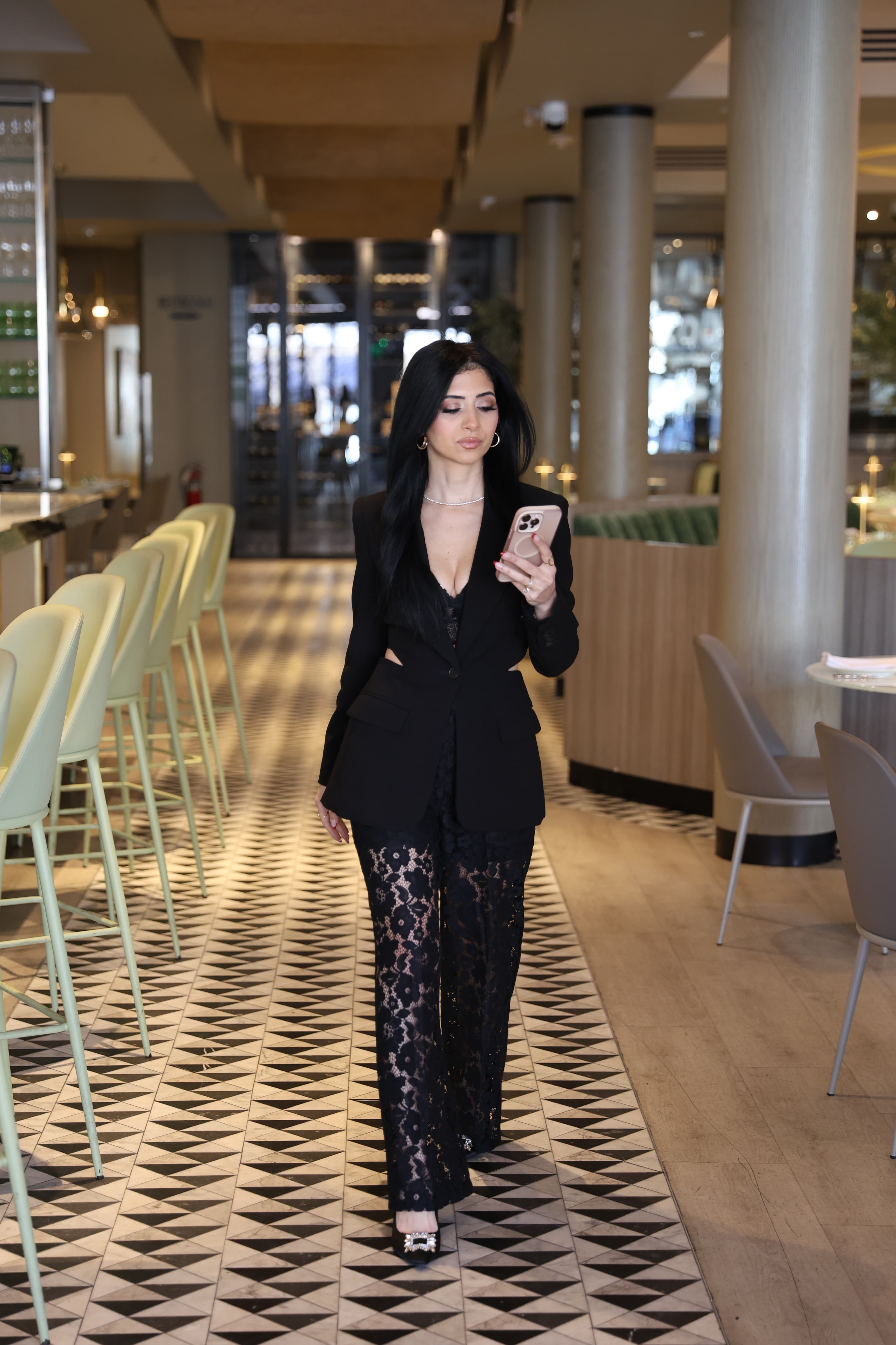 Jumana Yousif walking through a refined interior while reviewing her phone